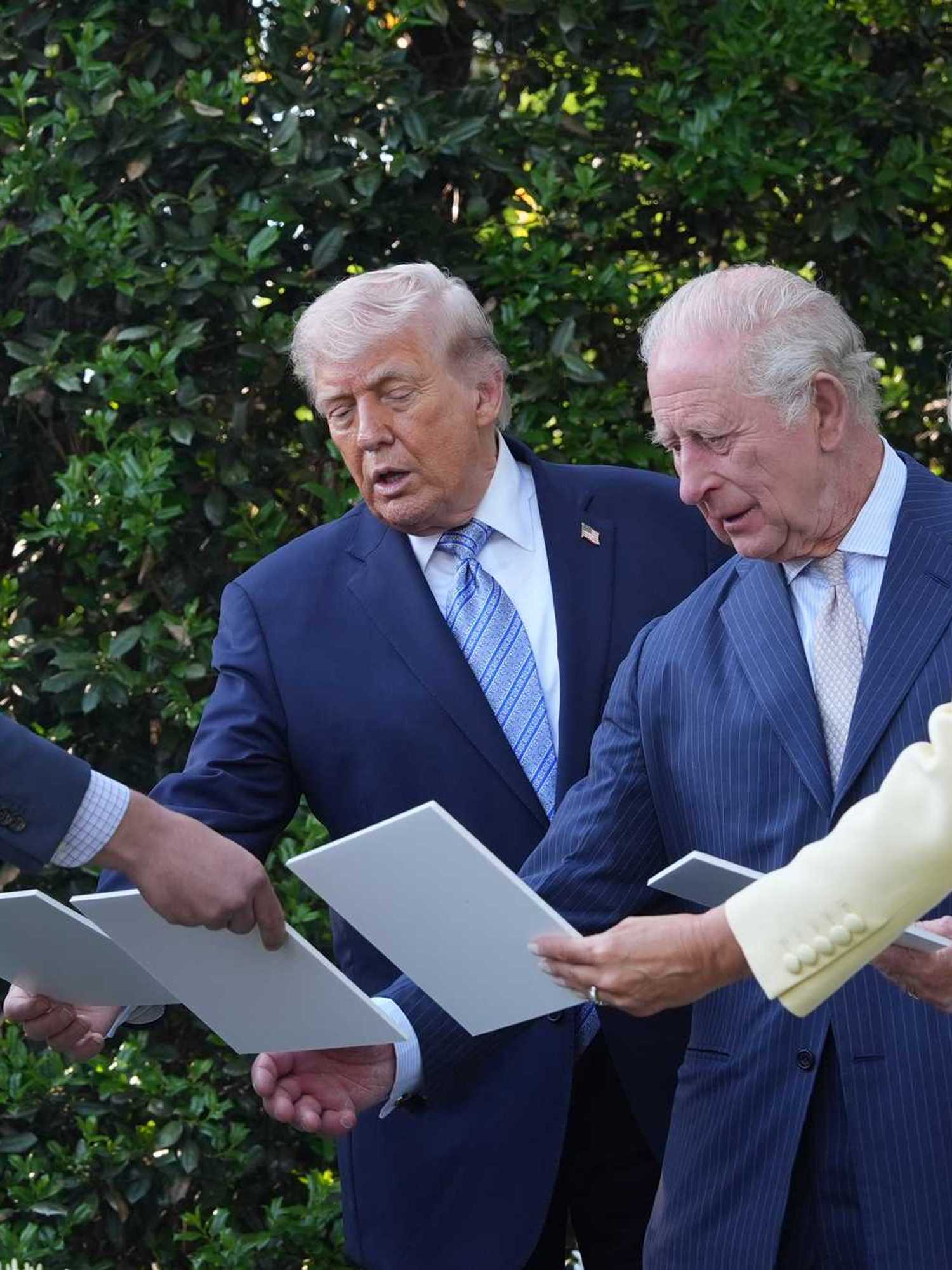 Donald Trump and King Charles III look at white cards at the White House beehives.