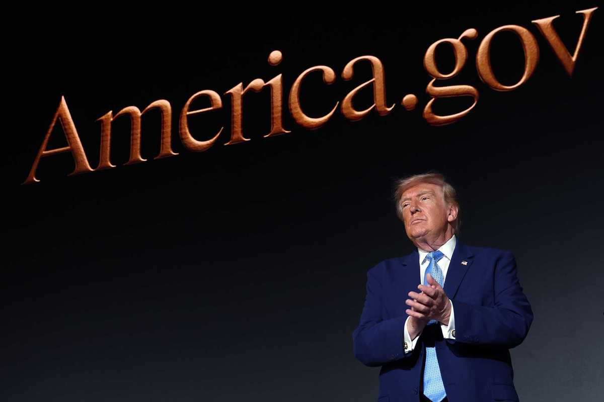 Donald Trump applauds in front of a giant screen with the words 'America.gov' on it.