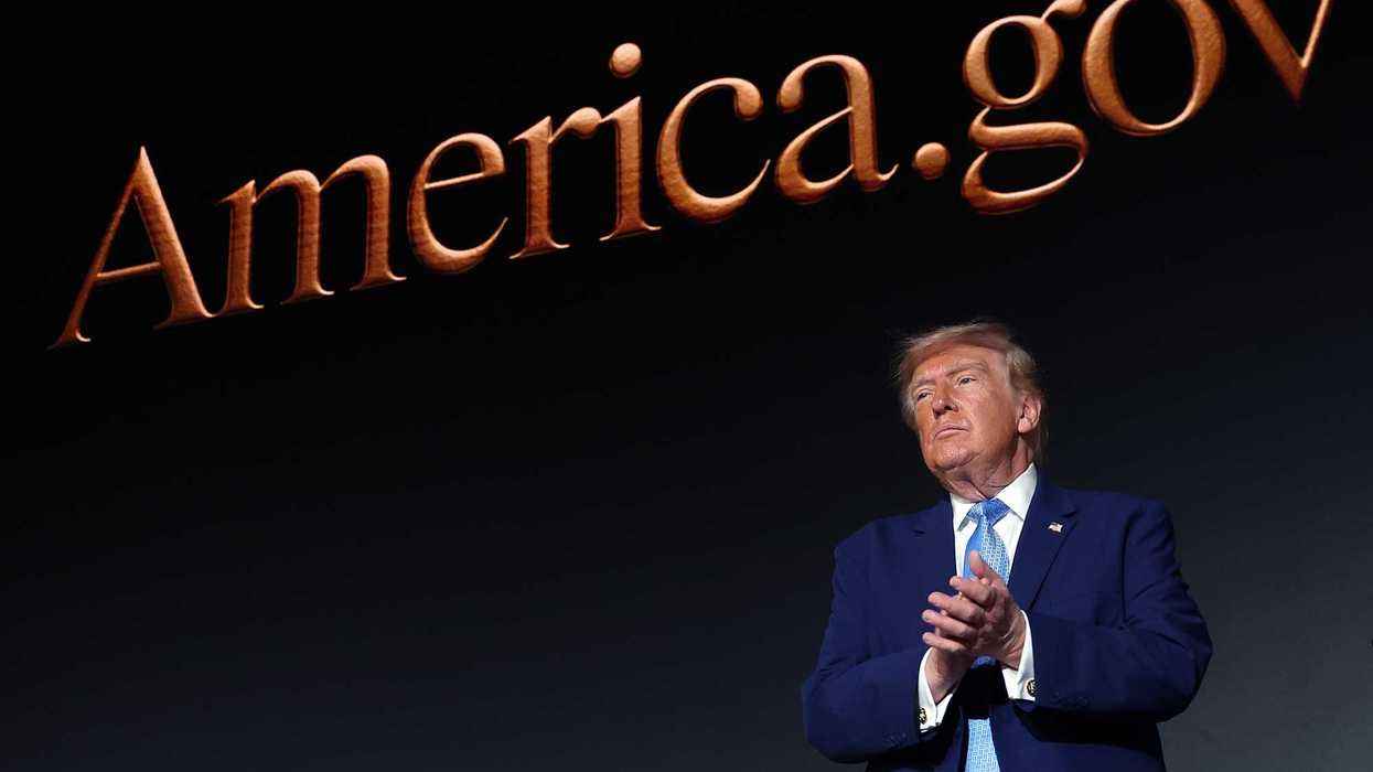Donald Trump applauds in front of a giant screen with the words 'America.gov' on it.