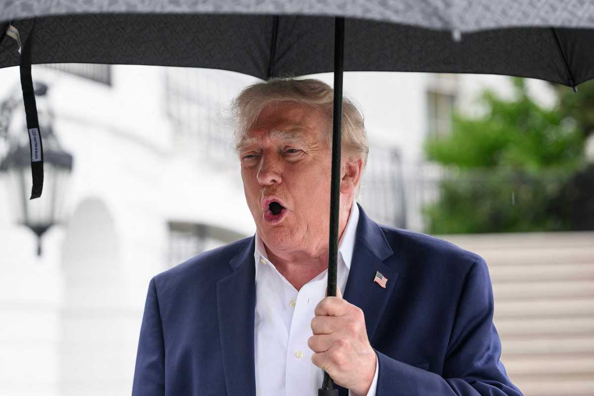 Donald Trump holding an umbrella and speaking to reporters outside the White House.