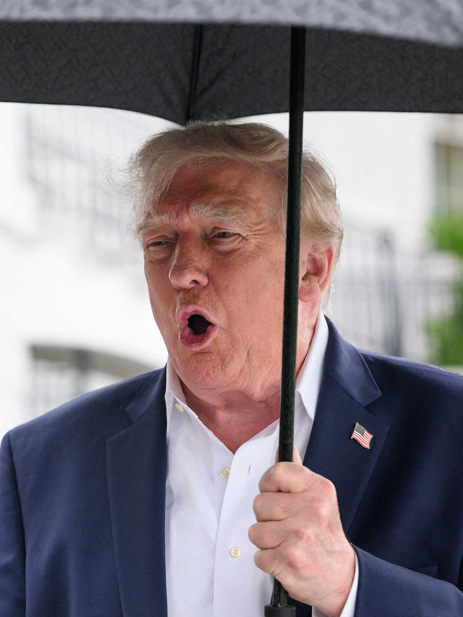 Donald Trump holding an umbrella and speaking to reporters outside the White House.