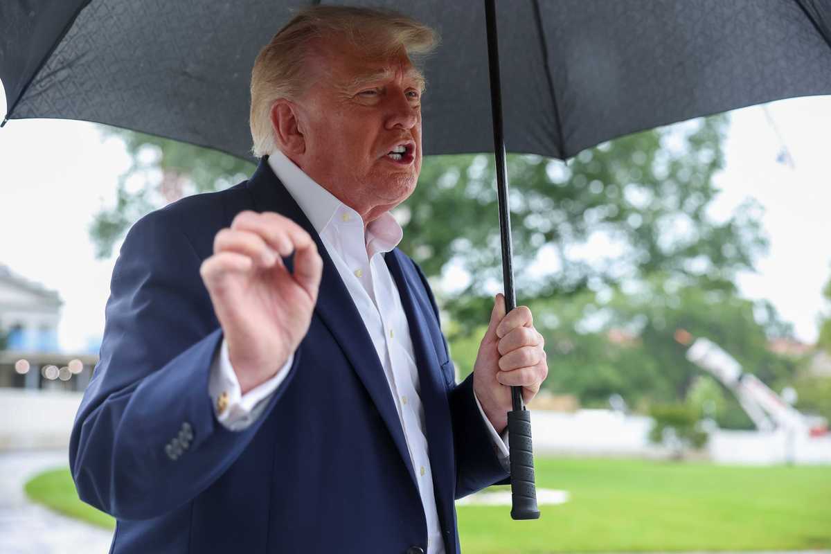Donald Trump holding an umbrella and speaking to reporters outside the White House.