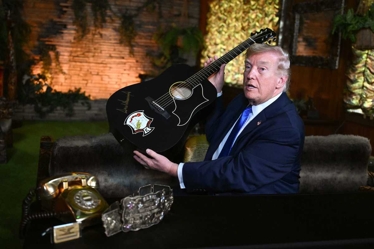 Donald Trump holds up a black acoustic guitar with his autograph on it in golden ink.