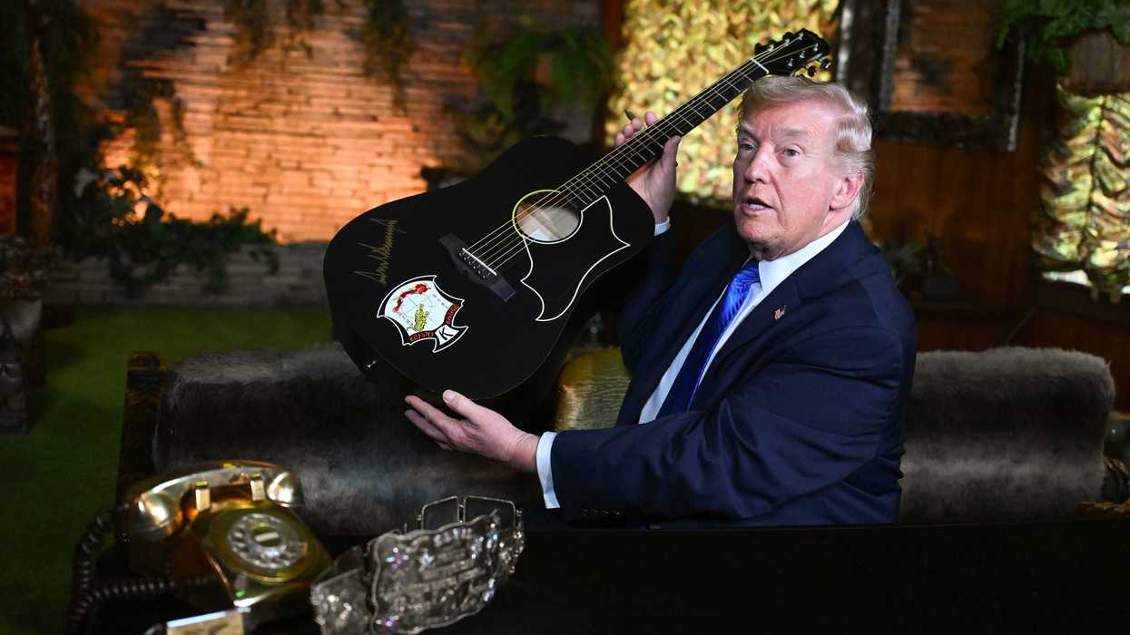 Donald Trump holds up a black acoustic guitar with his autograph on it in golden ink.