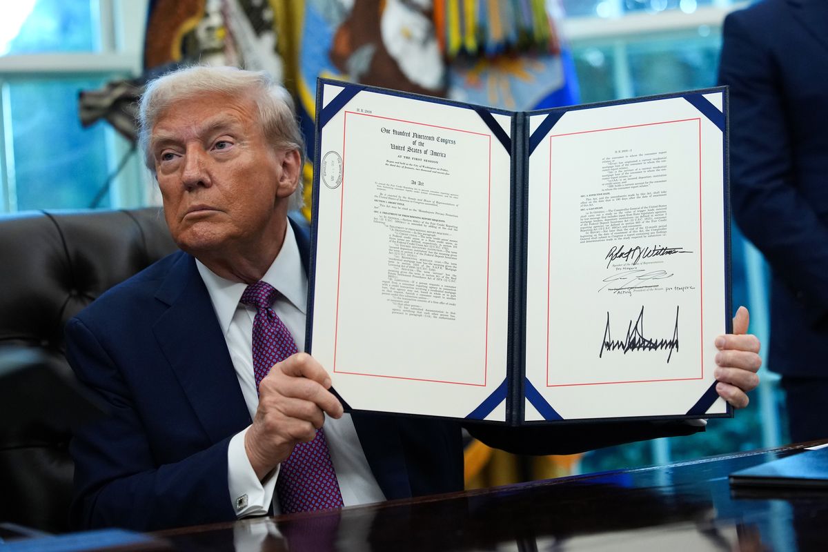 Donald Trump holds up a signed executive order behind his desk in the Oval Office.