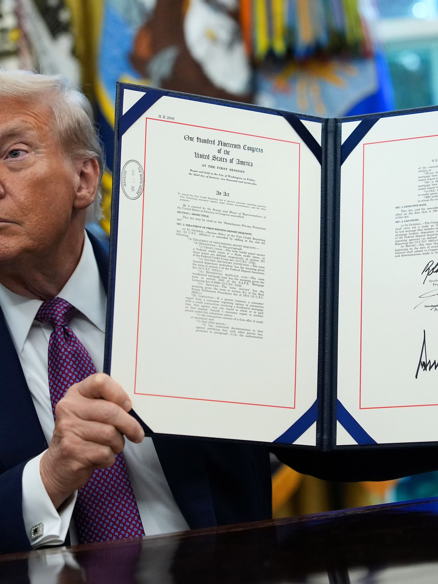 Donald Trump holds up a signed executive order behind his desk in the Oval Office.