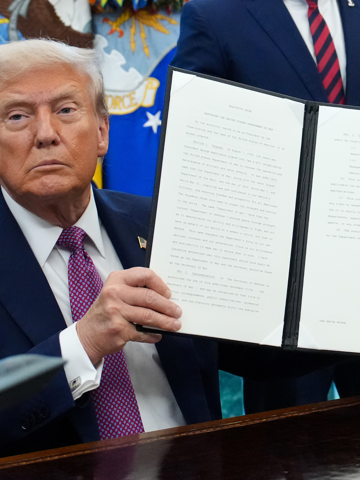 Donald Trump holds up a signed executive order in the Oval Office.