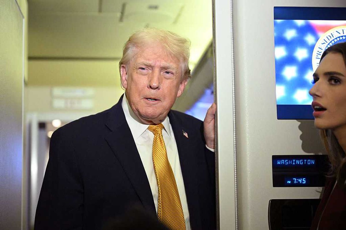 Donald Trump in a black suit and yellow tie talks to reporters on board Air Force One.