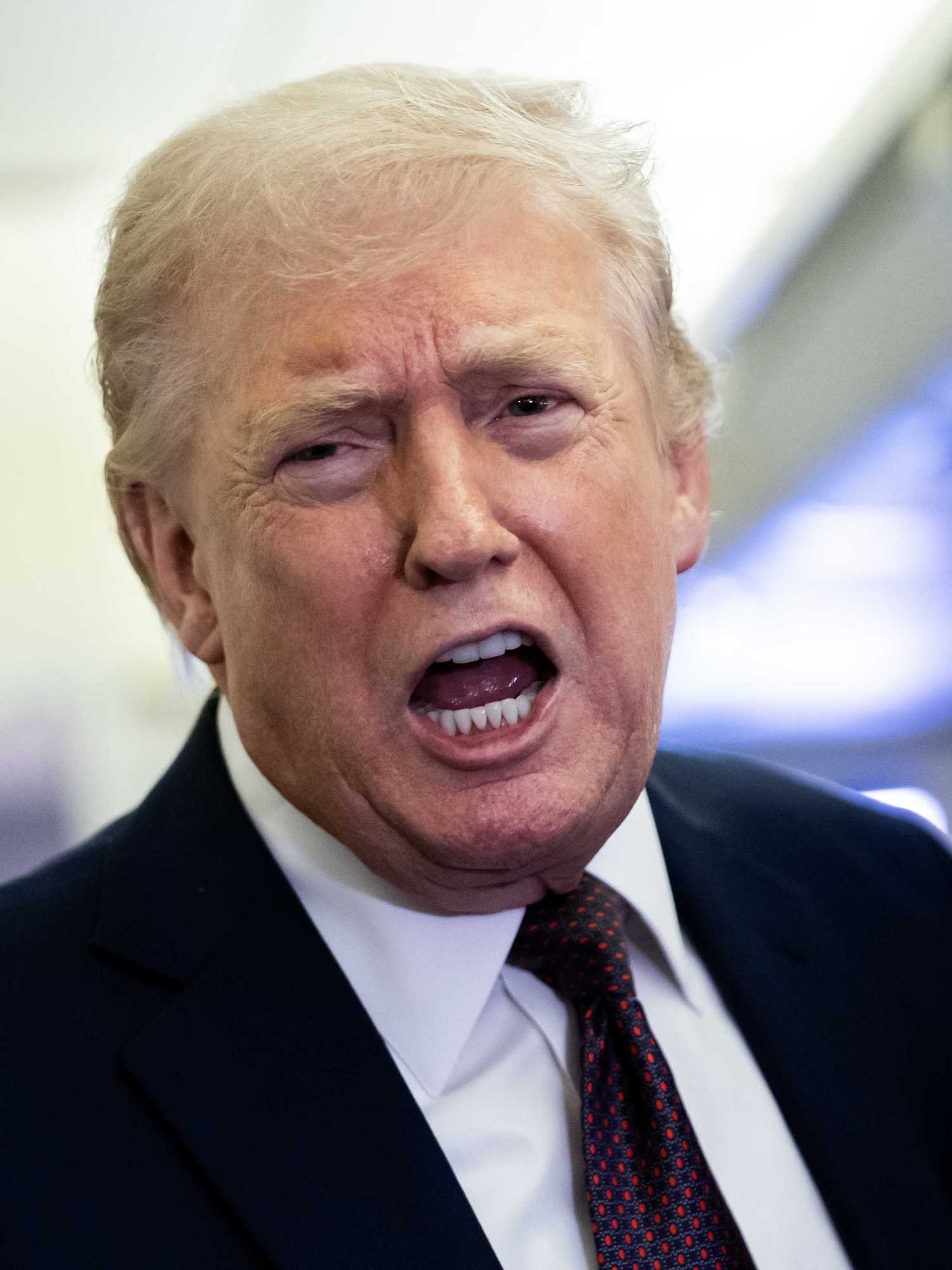 Donald Trump in a black suit speaks to reporters inside Air Force One.
