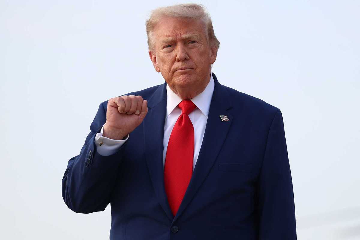Donald Trump in a blue suit and red tie raises a fist.