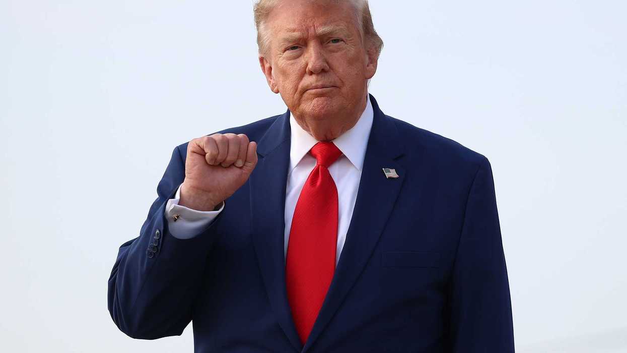 Donald Trump in a blue suit and red tie raises a fist.