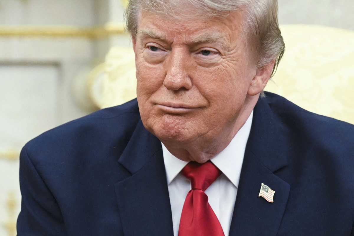 Donald Trump in a blue suit smiles in the Oval Office.