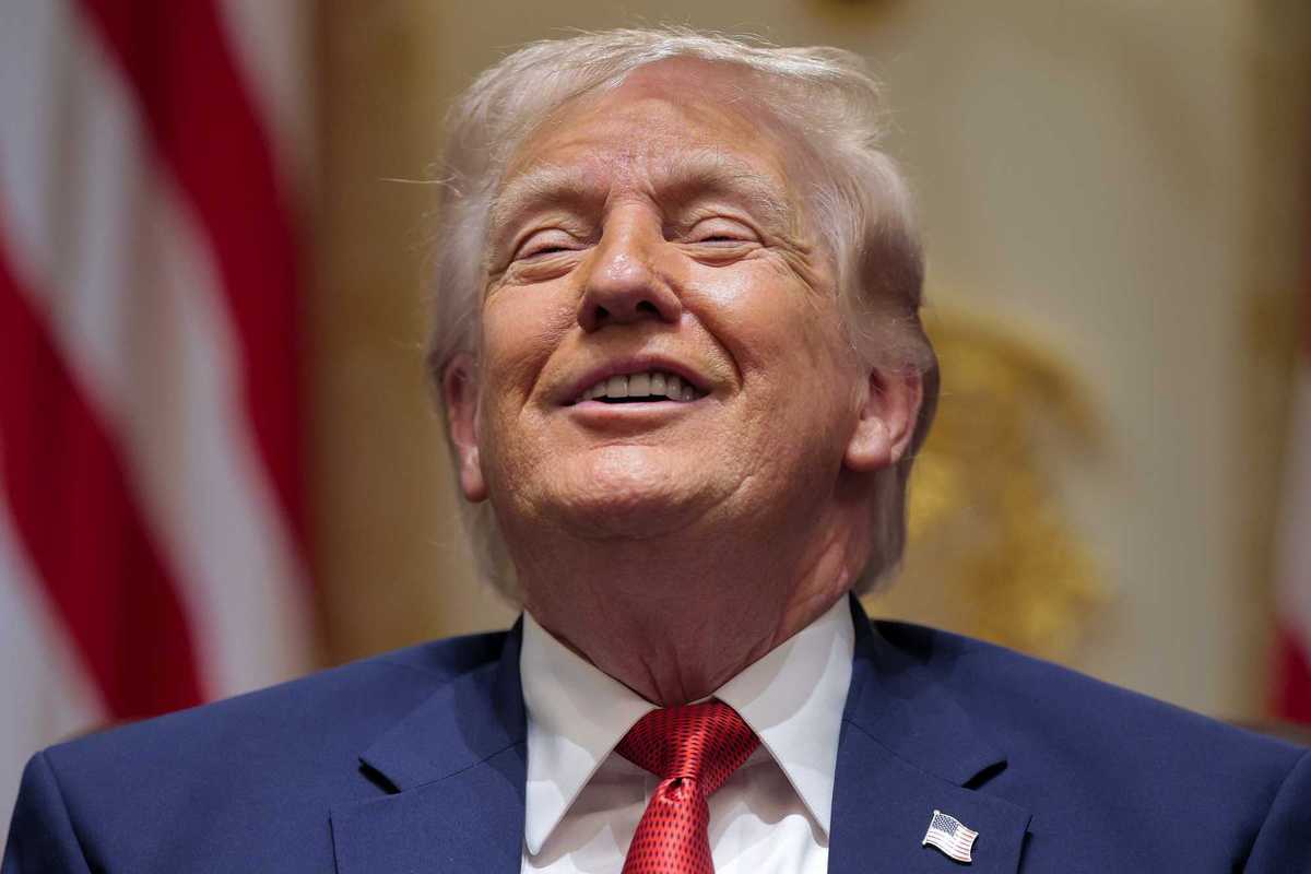 Donald Trump in a blue suit, tilting his head back slightly and smiling.
