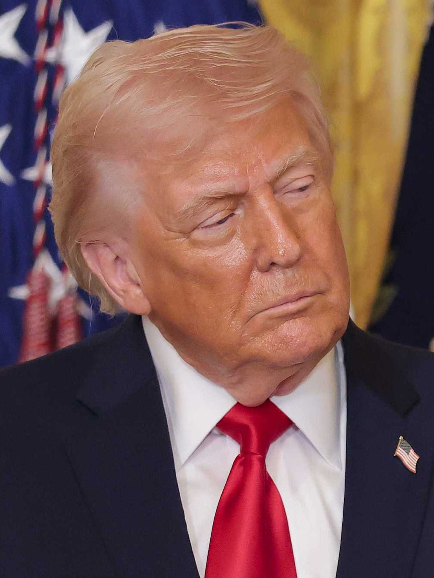 Donald Trump in a blue suit tilts his head slightly to the right as he looks to the left, with a neutral expression on his face.