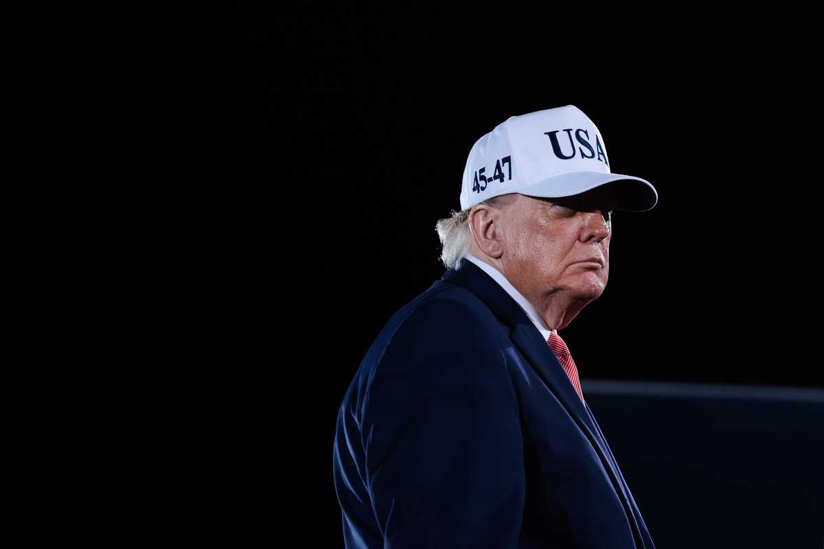 Donald Trump in a blue suit, wearing a white USA cap, at a rally in North Carolina.