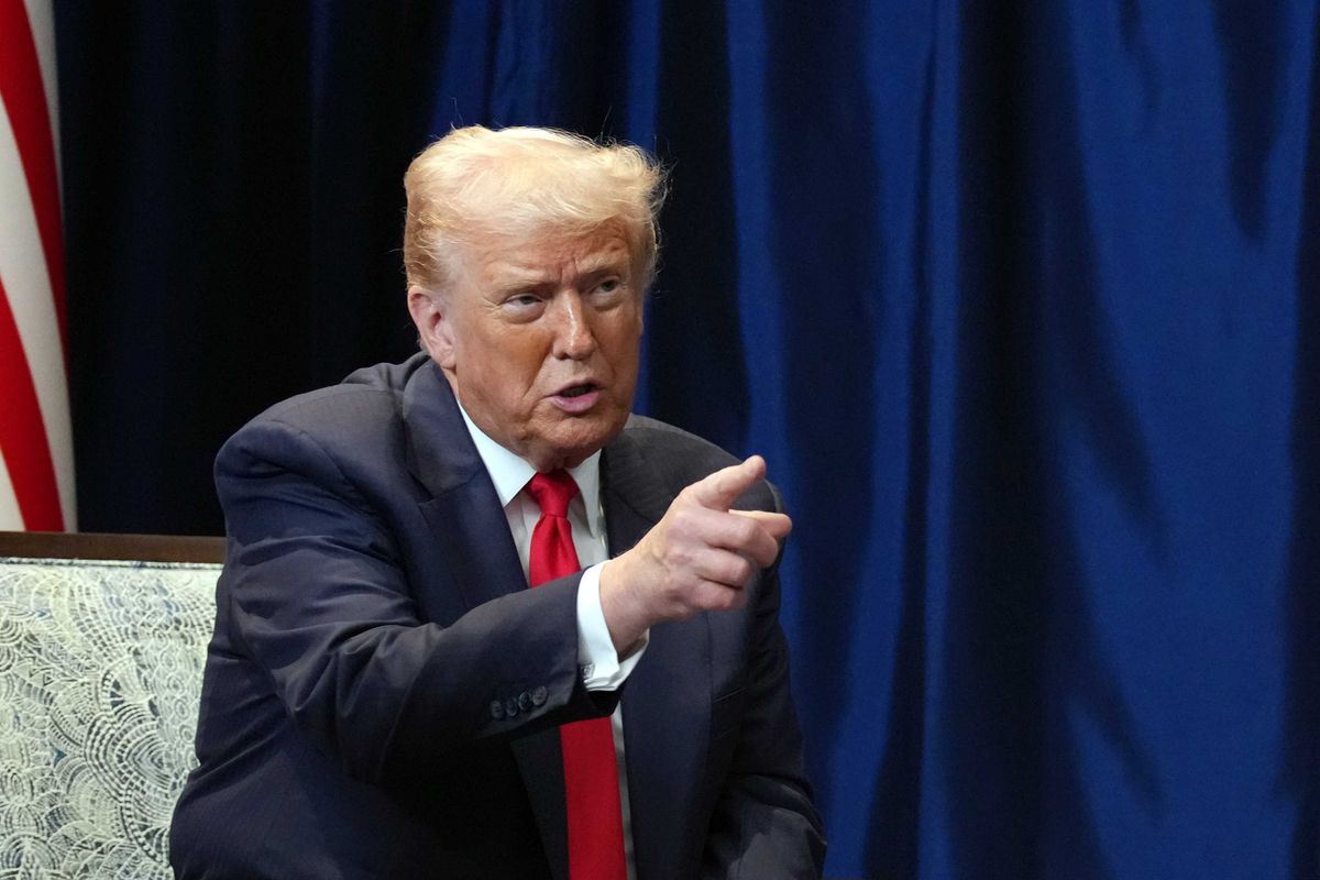 Donald Trump, in a dark blue suit and red tie, speaks and points with his right index finger at someone off-camera.