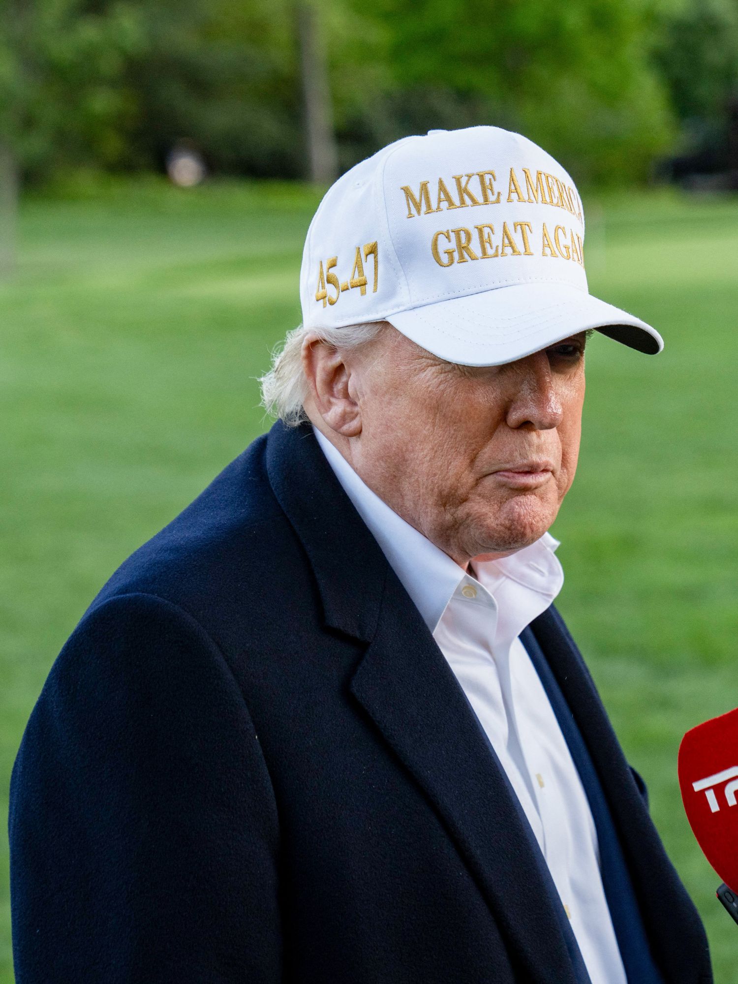 Donald Trump in a white Maga hat speaks to reporters on the White House green.