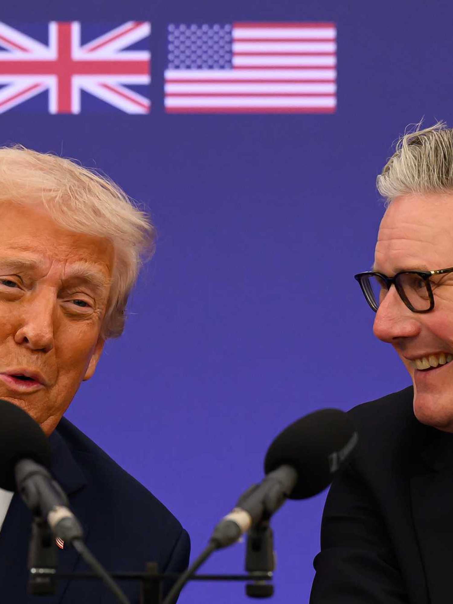 Donald Trump, left, and Keir Starmer, right as they speak into microphones in front of them. The UK and US flags are seen on a blue poster board behind them.