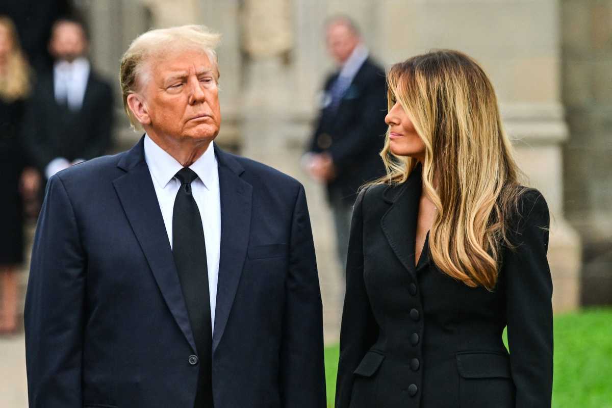 Donald Trump, left, looks ahead with a frowning facial expression, while Melania, right, with wavy blonde hair, turns her head right to look at him with a faint smile.