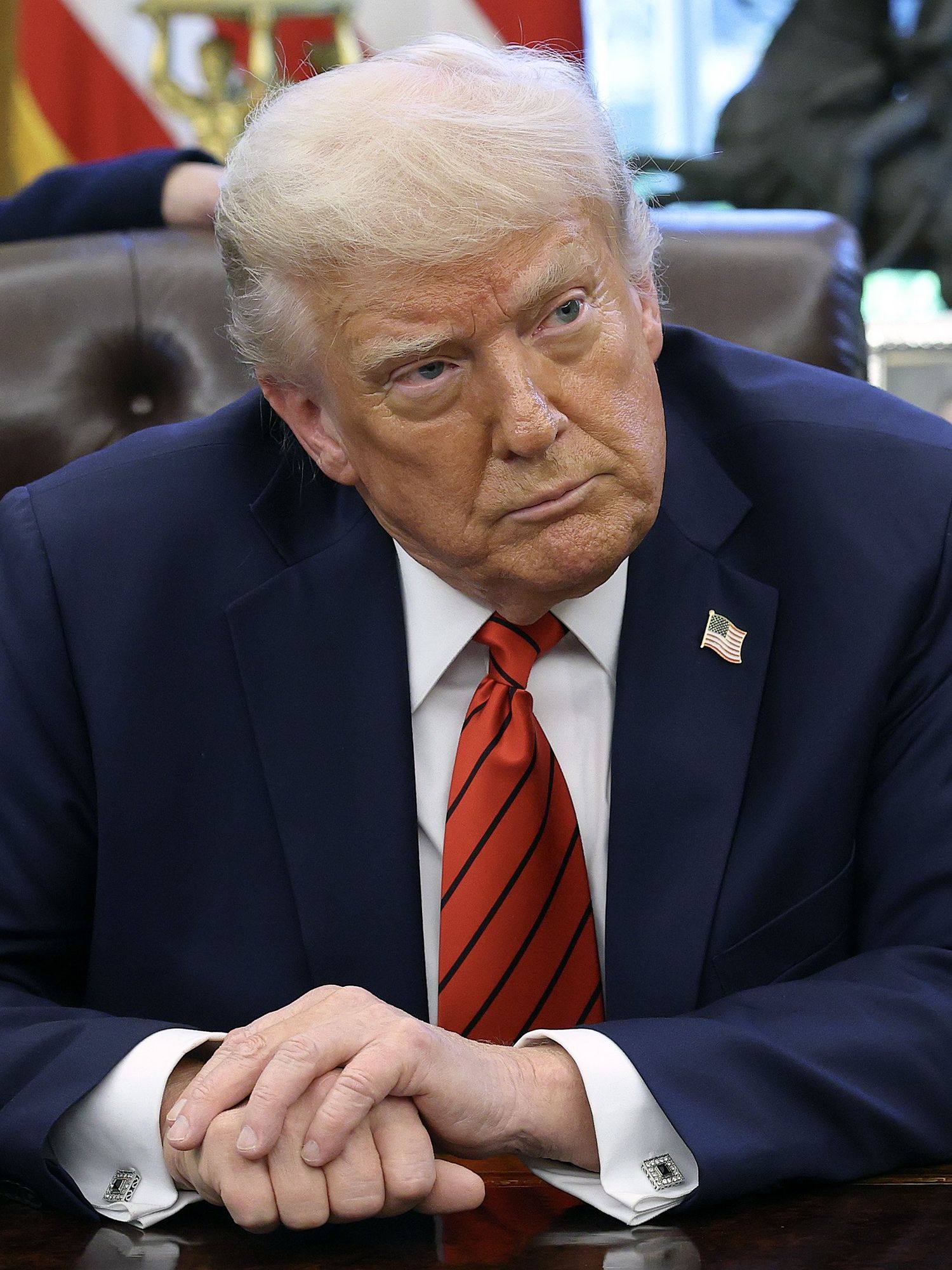 Donald Trump looks at reporters as he sits behind his desk in the Oval Office.