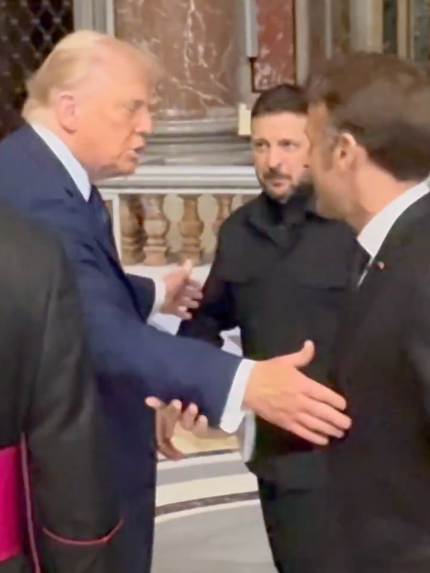 Donald Trump outstretches a hand to Emmanuel Macron inside St Peter's Basilica, with Volodymyr Zelensky in the background.