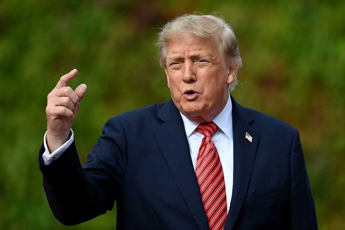 Donald Trump pointing with his right hand while speaking to reporters.