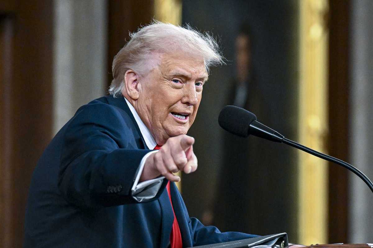 Donald Trump points and looks at something to his right while speaking into a microphone and standing behind a lectern in Congress. He's giving his State of the Union address.