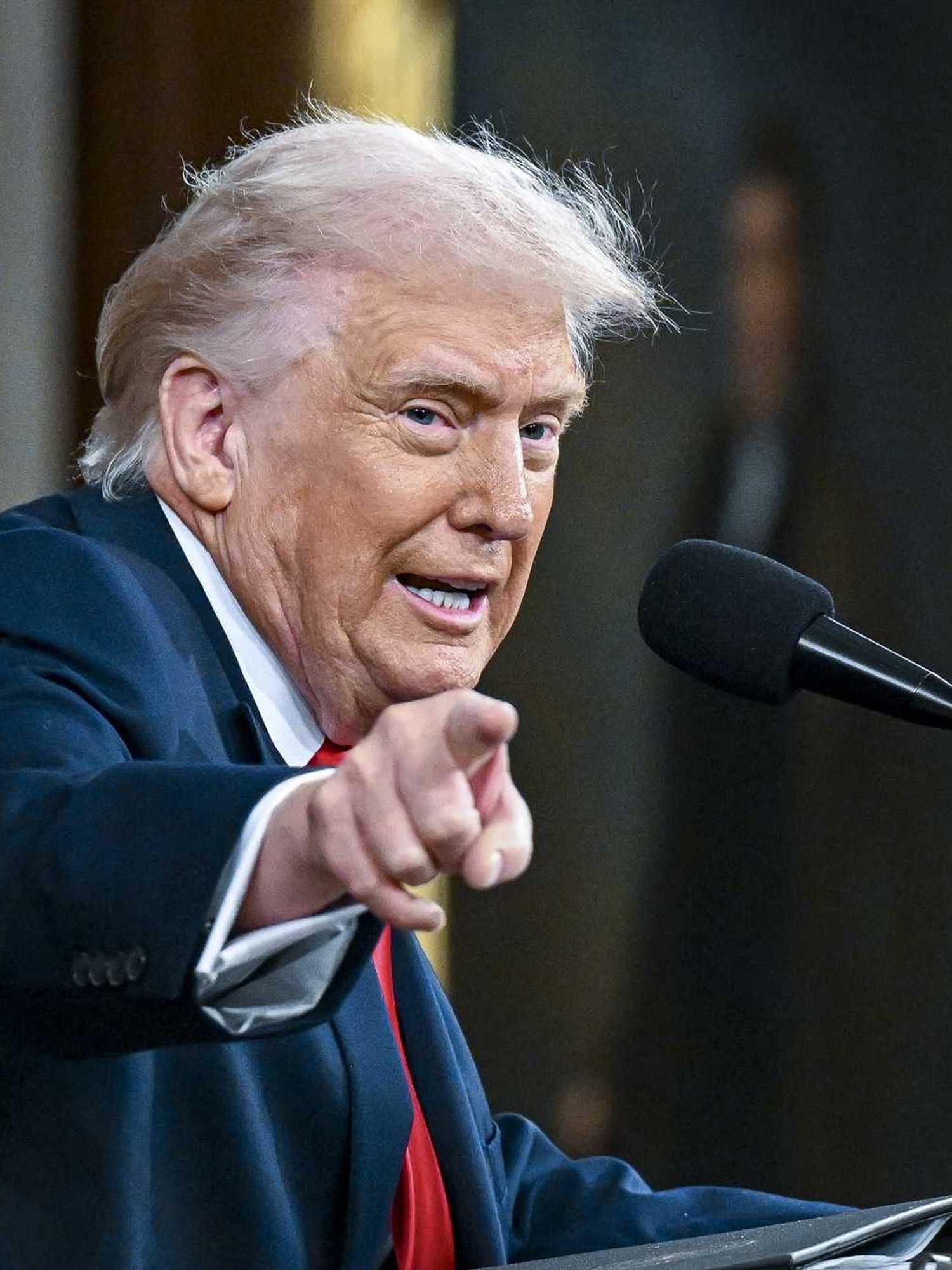 Donald Trump points and looks at something to his right while speaking into a microphone and standing behind a lectern in Congress. He's giving his State of the Union address.