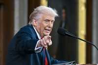 Donald Trump points and looks at something to his right while speaking into a microphone and standing behind a lectern in Congress. He's giving his State of the Union address.