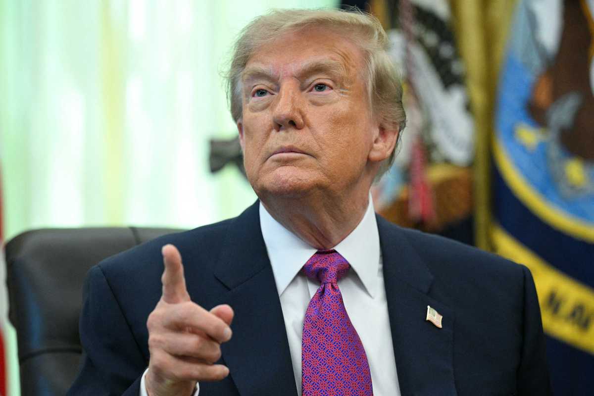Donald Trump points at someone off camera while taking questions from the media in the Oval Office.