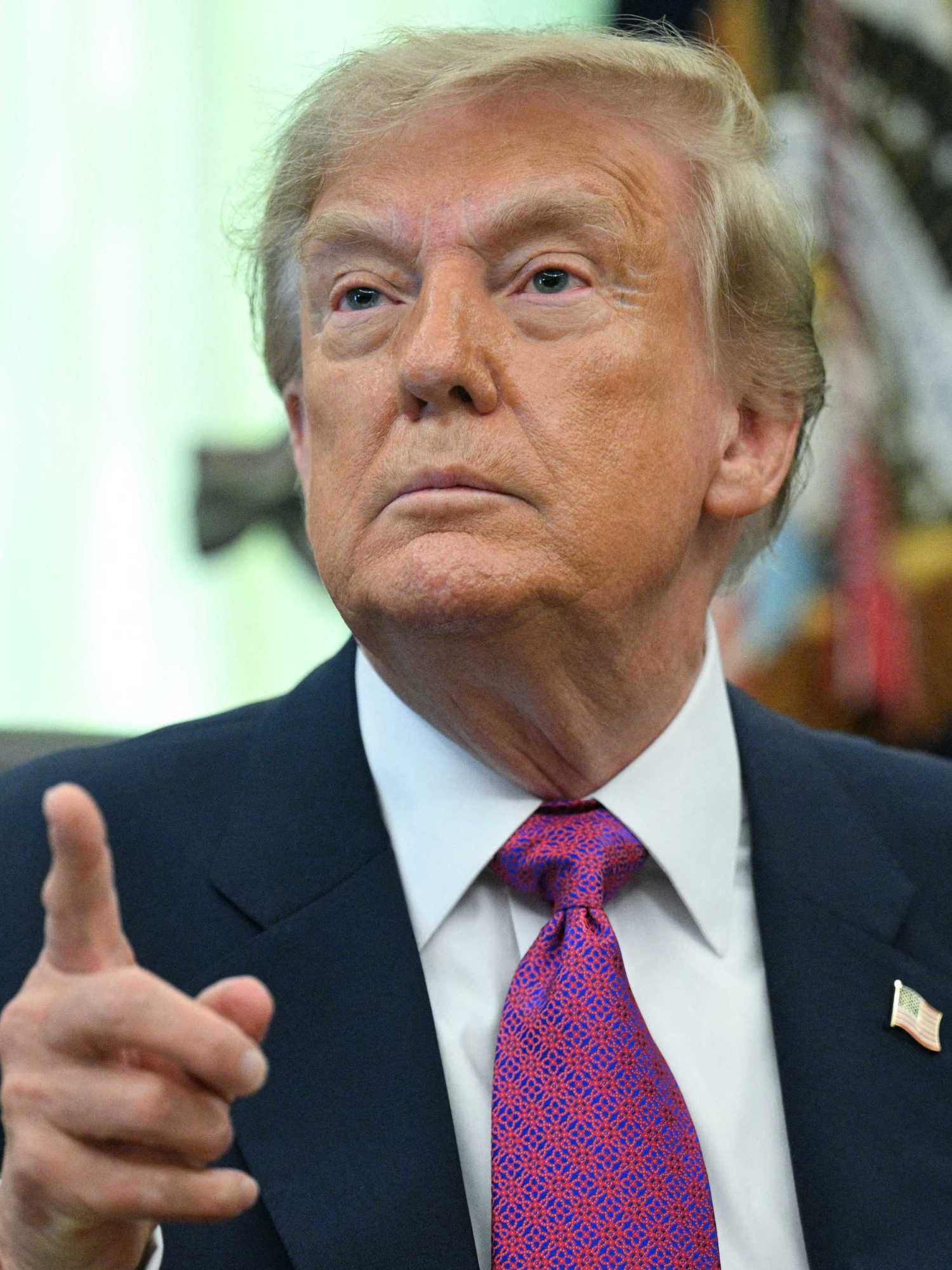 Donald Trump points at someone off camera while taking questions from the media in the Oval Office.