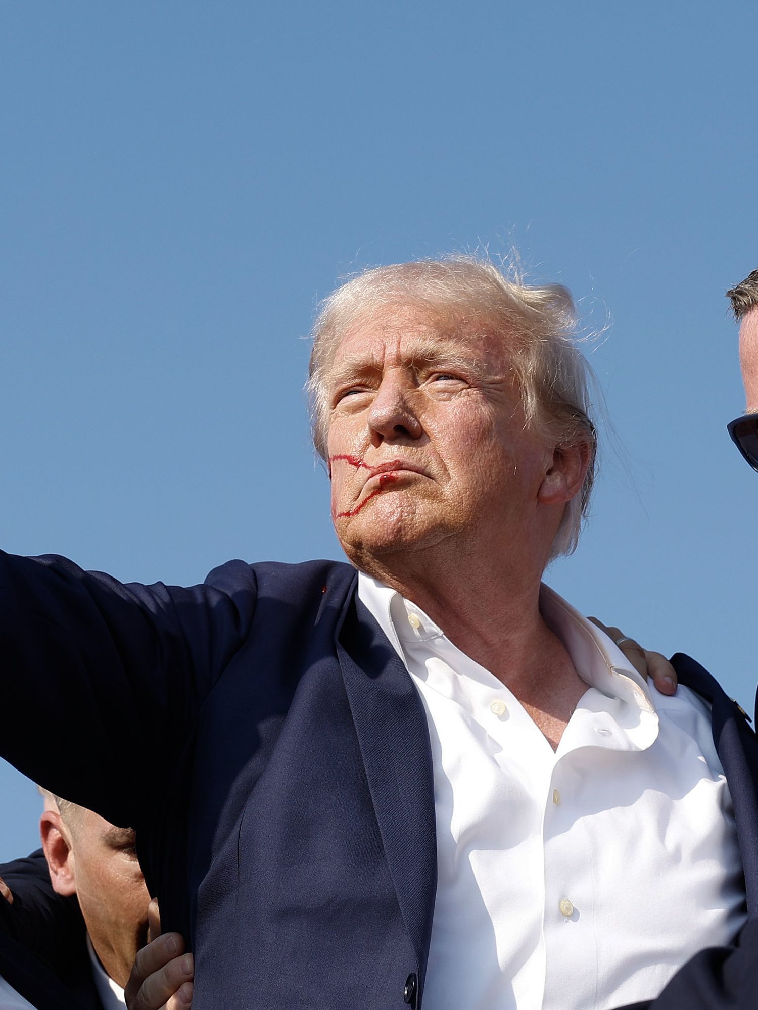 Donald Trump raises a fist in the air as he's carried away by secret service agents.
