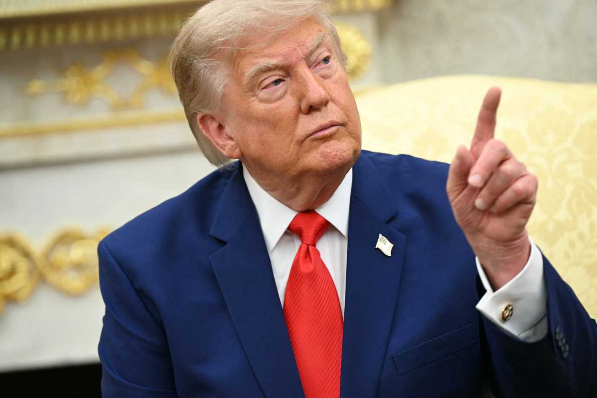 Donald Trump raises his left index finger while talking to reporters in the Oval Office.