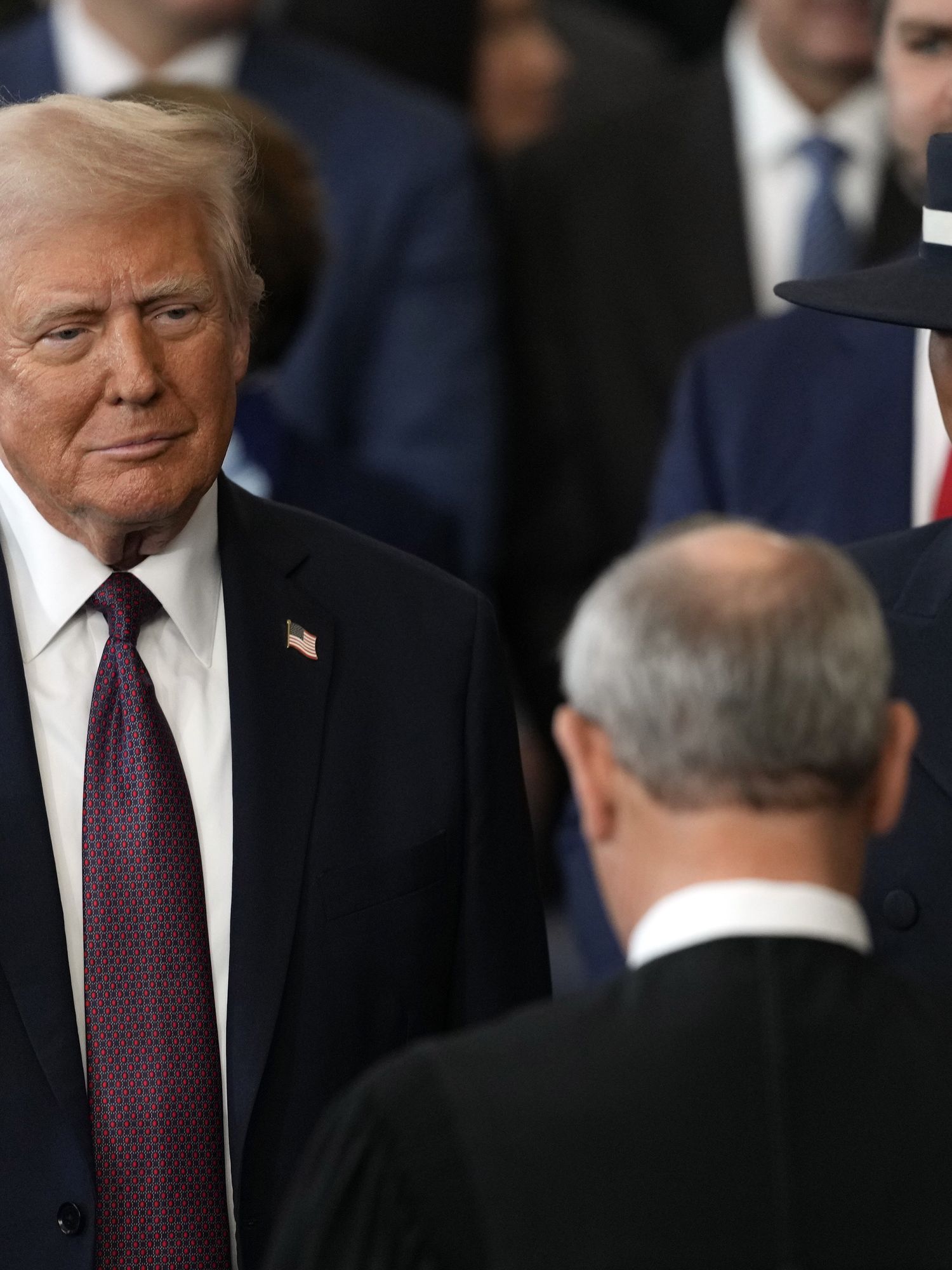 Donald Trump raises his right hand to swear the oath at his inauguration ceremony. Melania is to his left, with a neutral expression on her face.