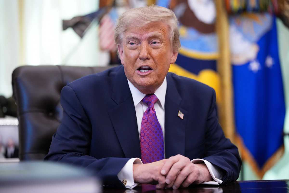 Donald Trump sits at the Resolute Desk in the Oval Office, talking to reporters.