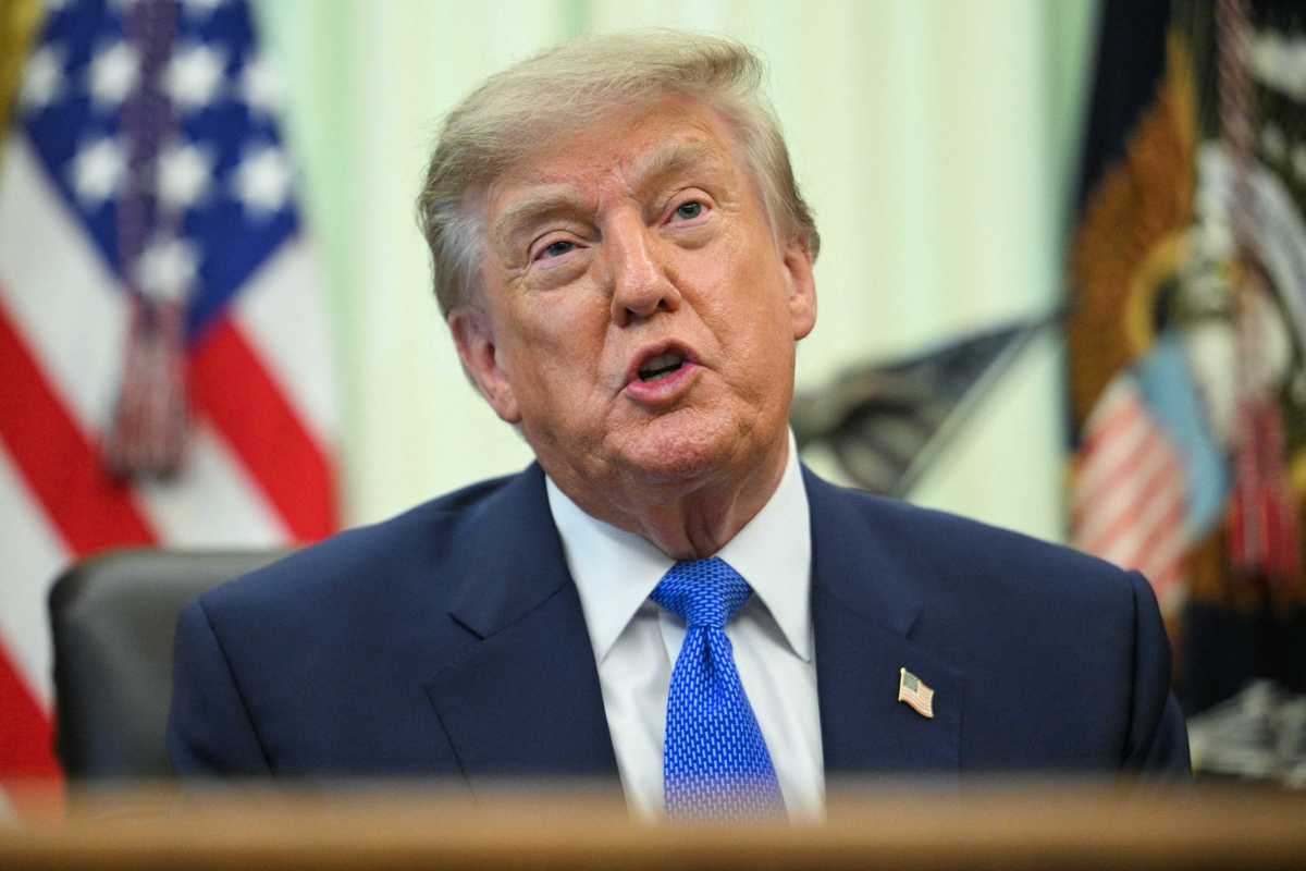 Donald Trump sits behind the Resolute Desk in the Oval Office, talking to reporters.