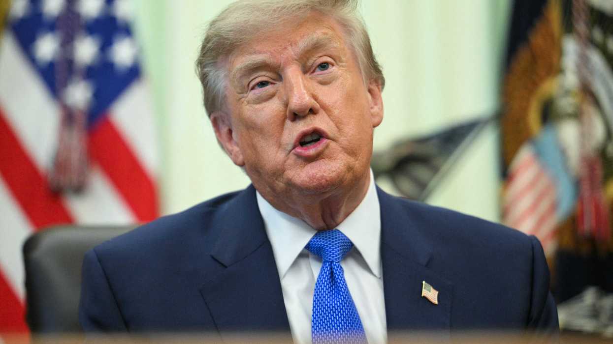 Donald Trump sits behind the Resolute Desk in the Oval Office, talking to reporters.