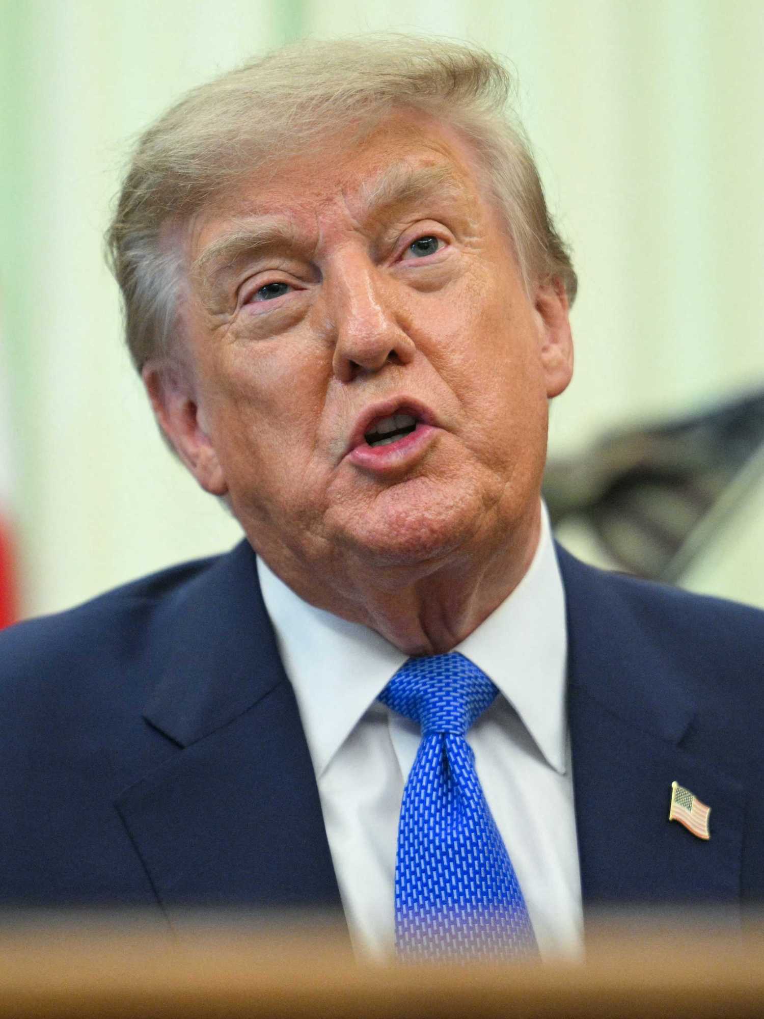 Donald Trump sits behind the Resolute Desk in the Oval Office, talking to reporters.