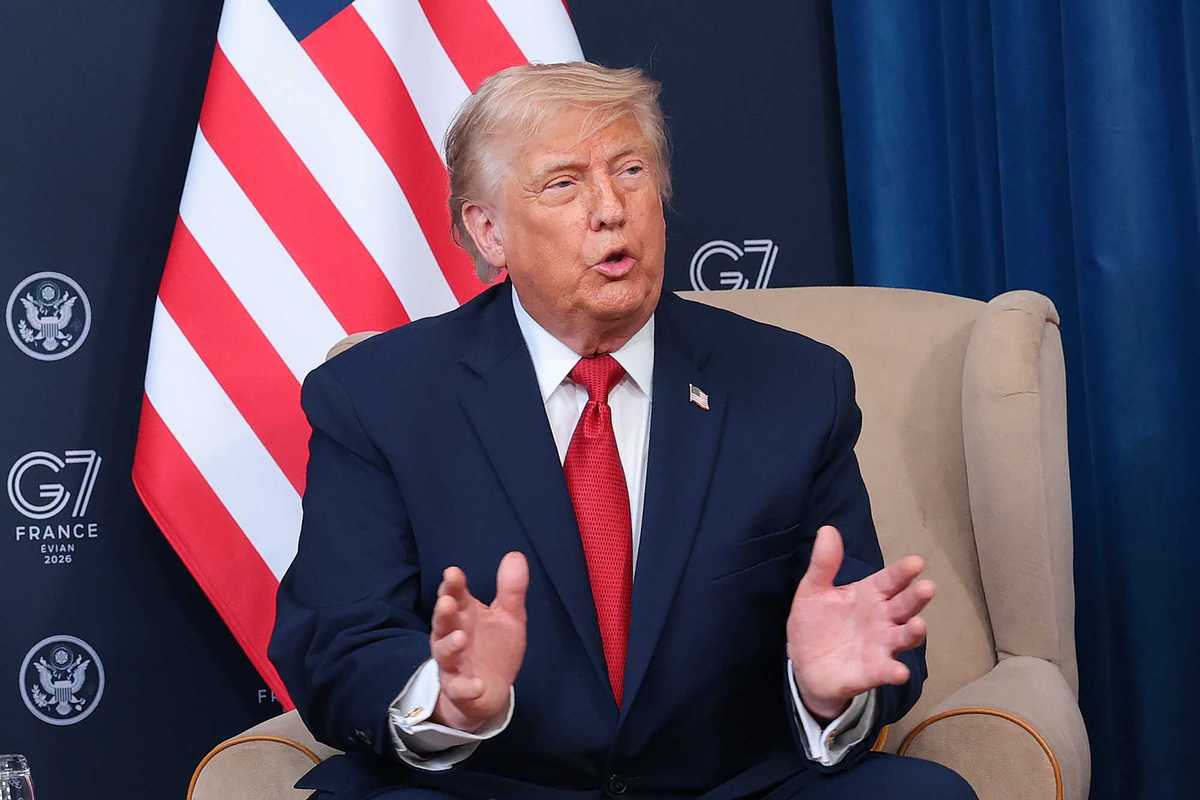 Donald Trump sits in a cream armchair and speaks to reporters in front of an American flag at the G7 in France.