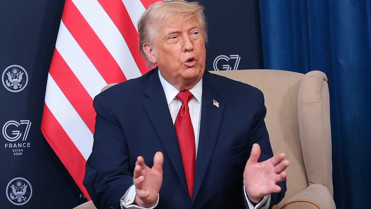 Donald Trump sits in a cream armchair and speaks to reporters in front of an American flag at the G7 in France.