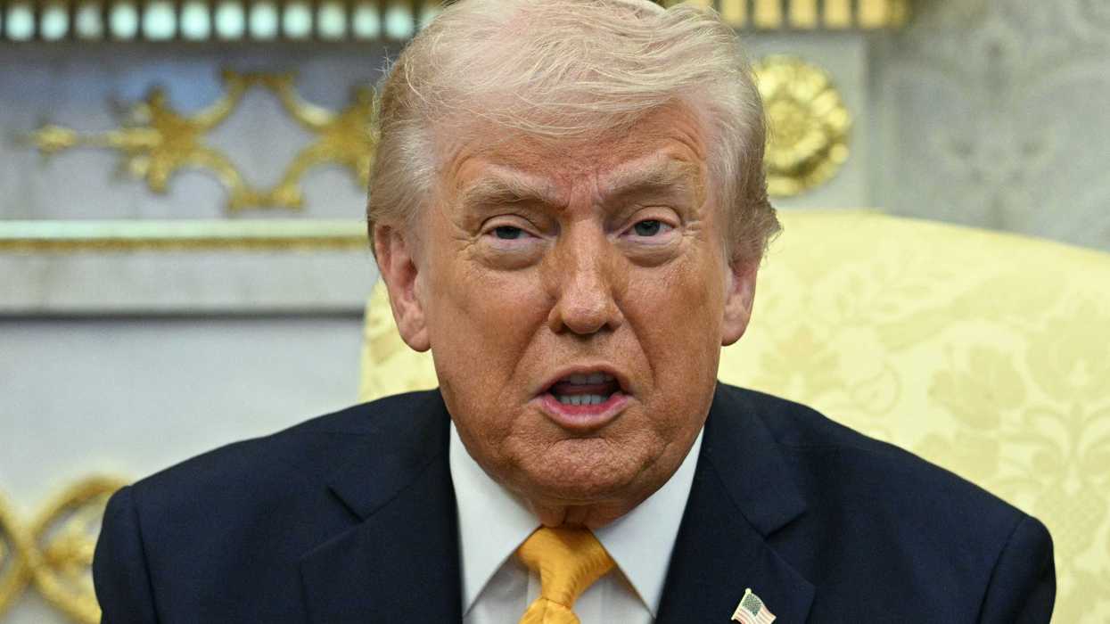 Donald Trump sits in a cream chair and speaks in the Oval Office.