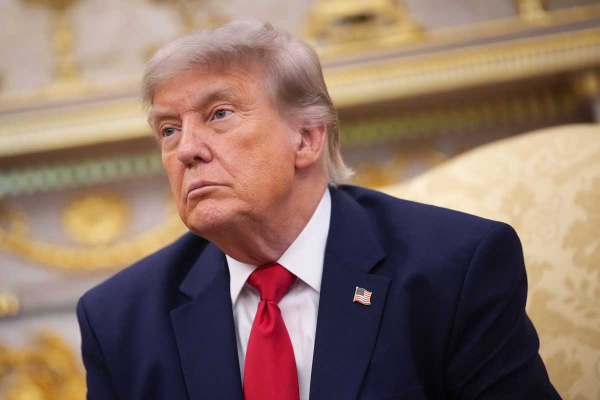 Donald Trump sits in the Oval Office wearing a blue suit and red tie.