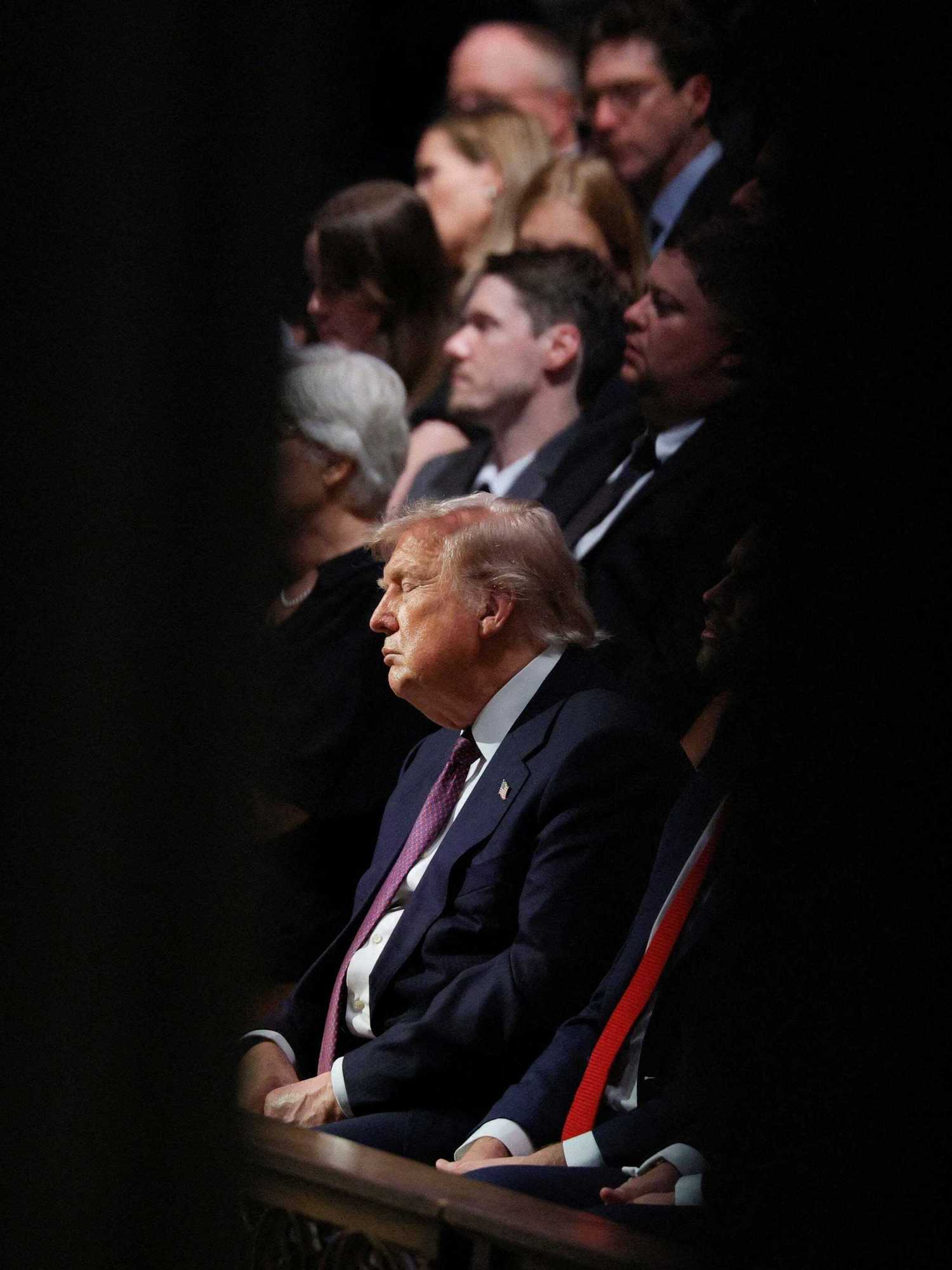 Donald Trump sits in wooden seating at the funeral for Lindsey Graham, with his eyes closed.