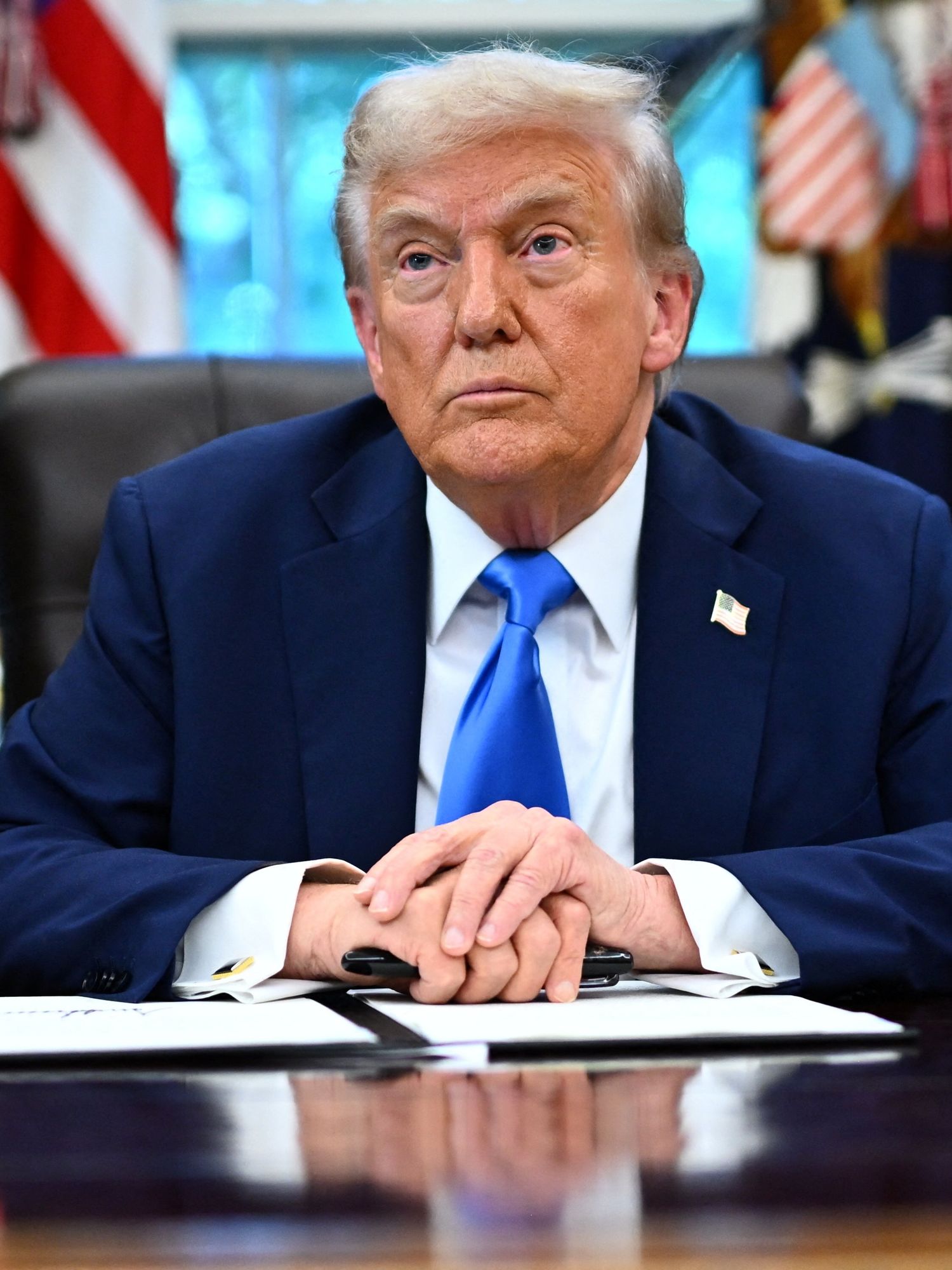 Donald Trump sitting at his Oval Office desk with an executive order open in front of him.