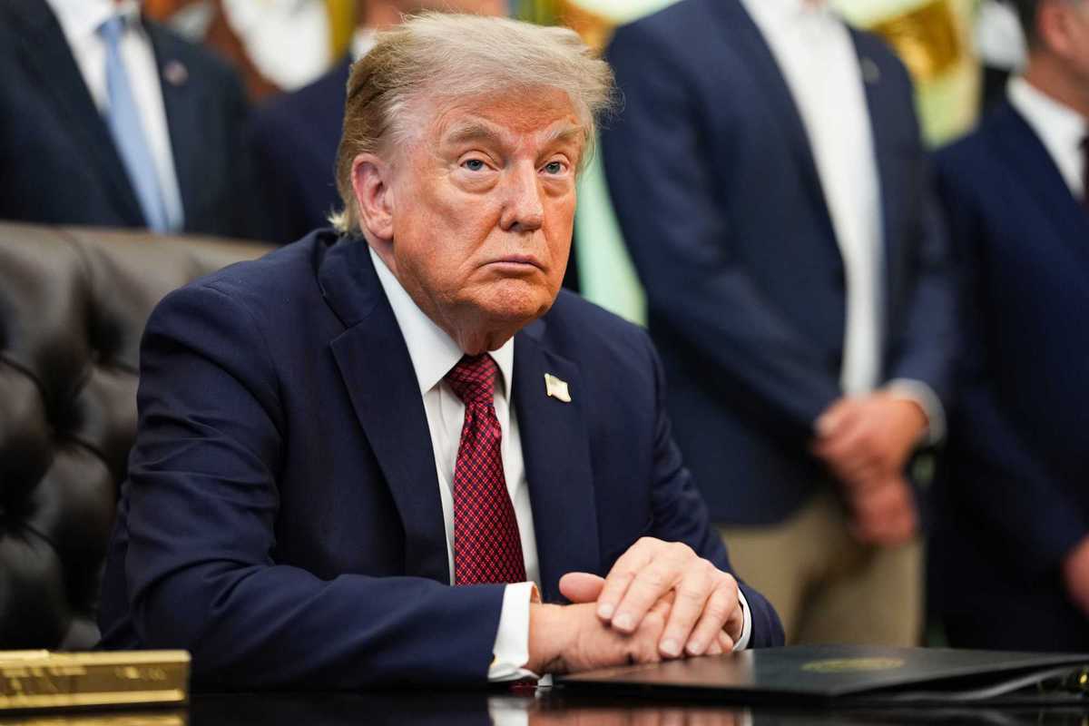 Donald Trump sitting at the Resolute Desk in the Oval Office of the White House.