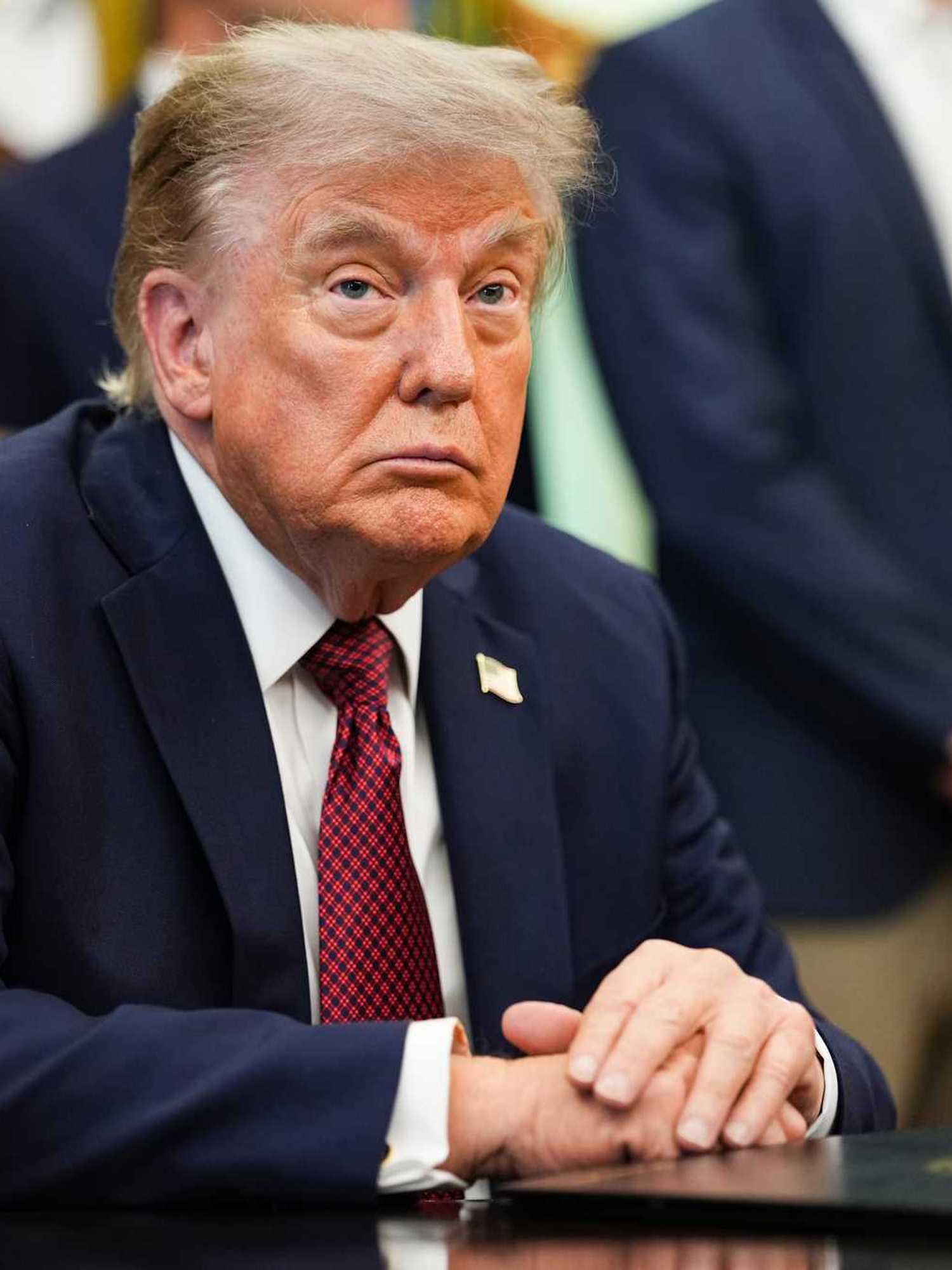 Donald Trump sitting at the Resolute Desk in the Oval Office of the White House.