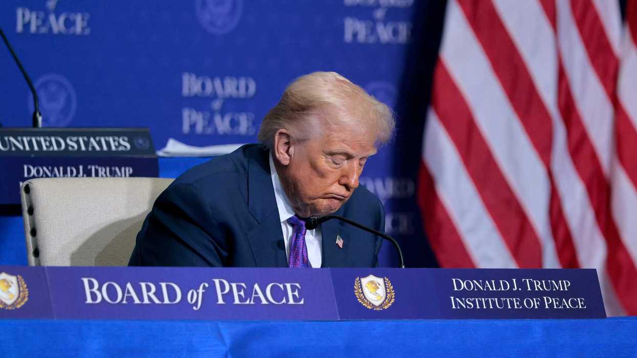 Donald Trump sitting behind a blue desk with 'Board of Peace' and 'Donald J. Trump Institute of Peace' signage on it. Trump has his head lowered, and appears to be asleep.