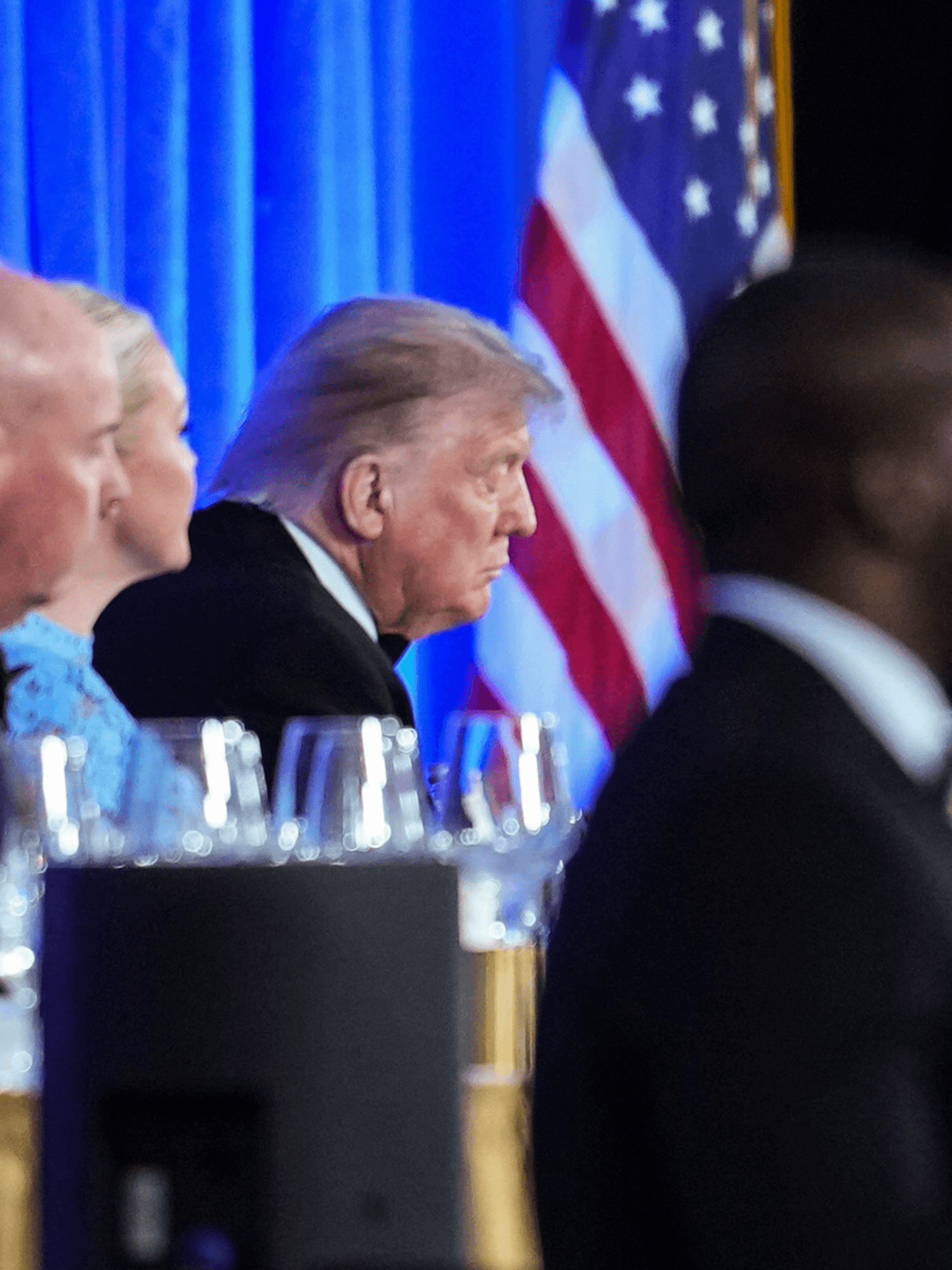 Donald Trump sitting behind a table at the White House Correspondents' Dinner, seemingly with his eyes closed.