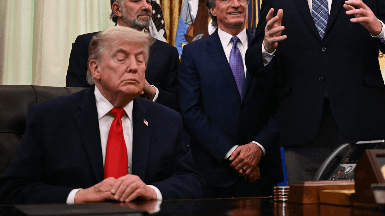 Donald Trump sitting behind the Resolute Desk in the Oval Office, appearing to have his eyes closed.