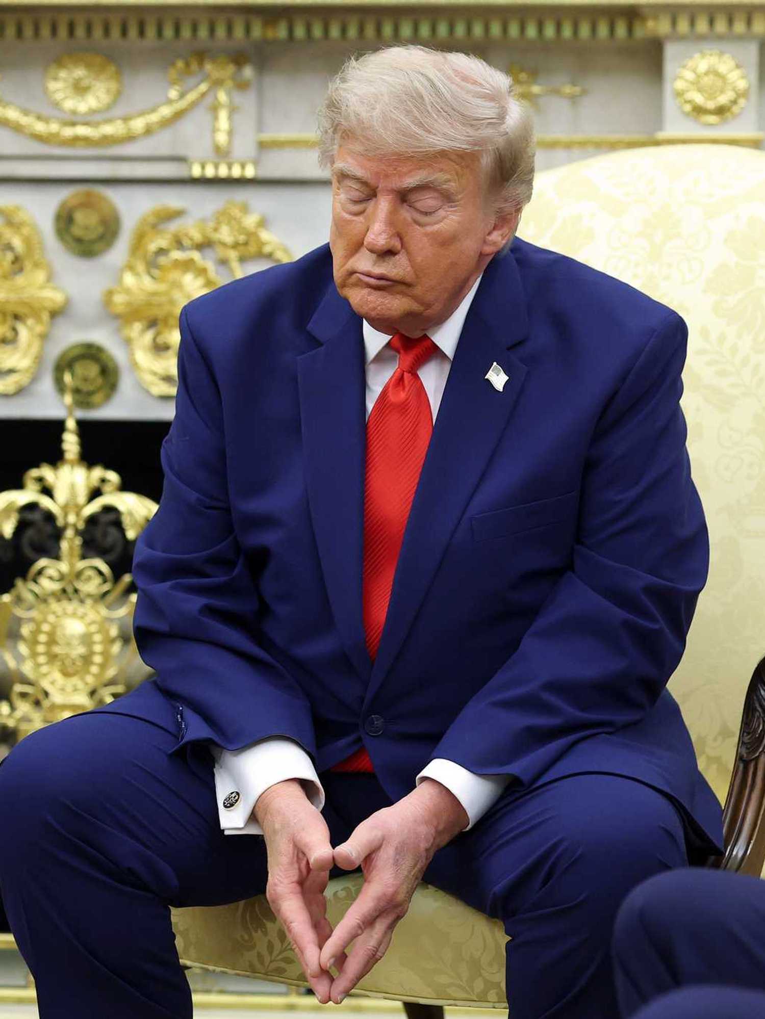 Donald Trump sitting in a cream chair in the Oval Office, with his eyes closed.